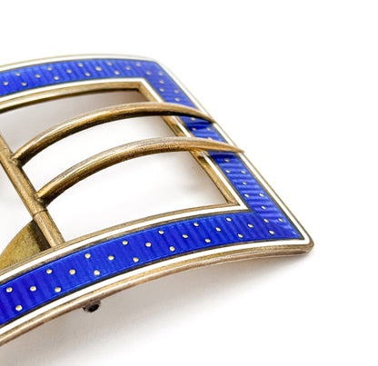 Close crop on one corner of the enamelled face, the gold dots and ribbed guilloché texture under the blue enamel clearly visible beside the pale white border and the two curved tongues crossing the opening.
