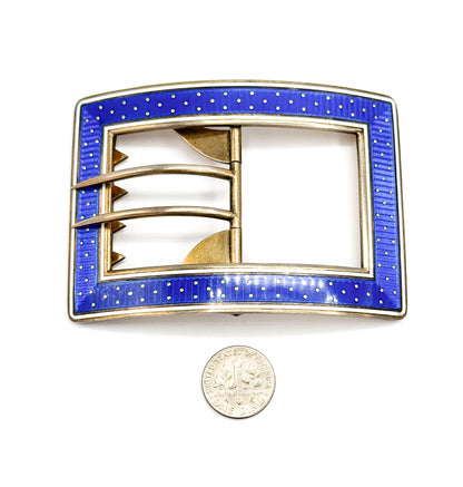The buckle flat and face-up beside a dime, which shows its size, with the blue enamel band of gold dots framing the open centre, hinged tongue and notched bars.