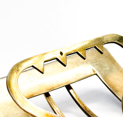 Extreme close-up of the gold-washed silver underside, where a zigzag-notched bar meets the curved frame and a tiny struck mark sits between two of the points.