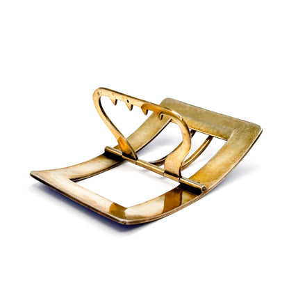 The underside of the whole buckle in gold-washed silver, its plain curved frame enclosing the hinged tongue and the zigzag-notched bar, with no enamel visible from this side.
