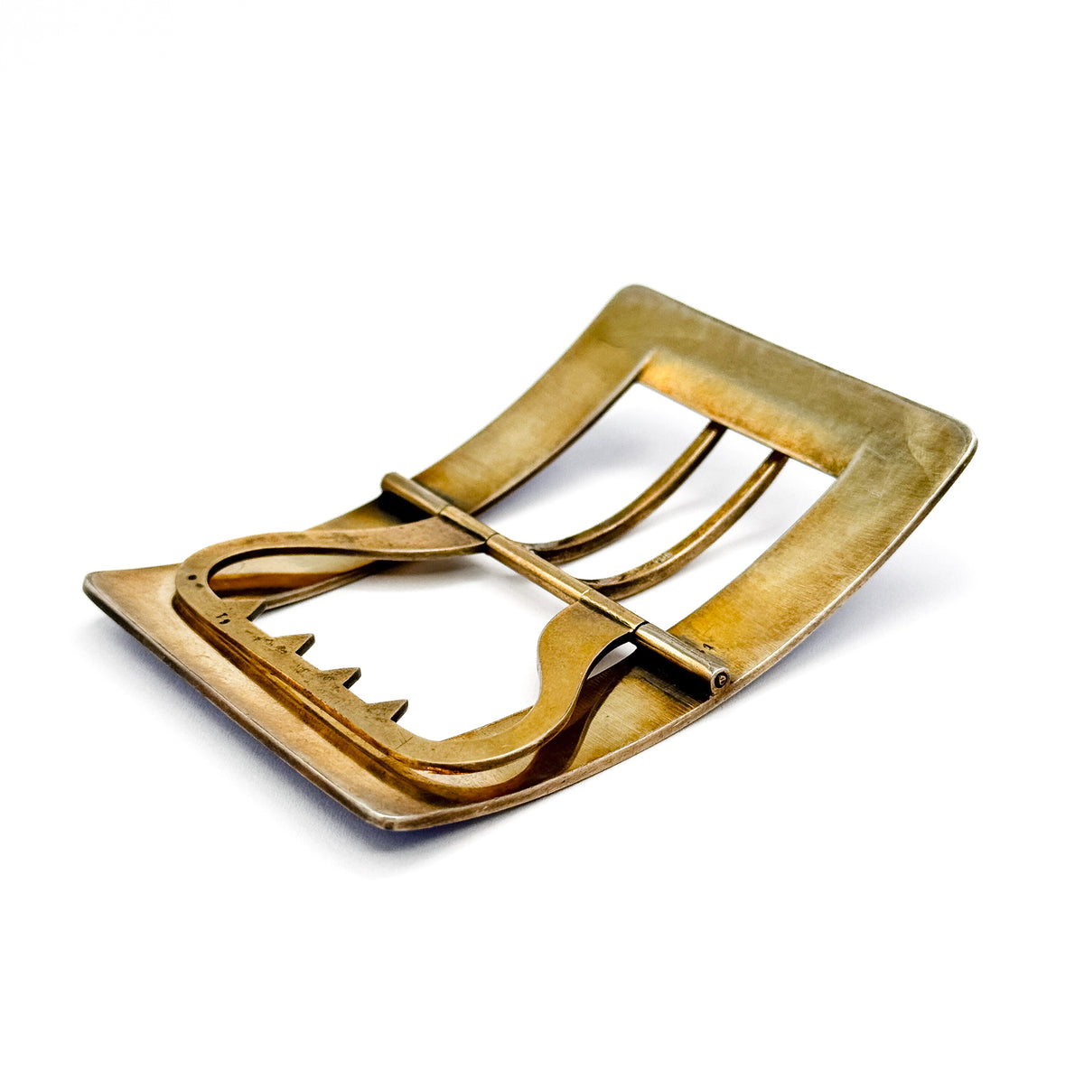 Low three-quarter view of the gold-washed underside, where the curve of the frame rises in profile and the hinge pins at either end of the tongue catch the light.