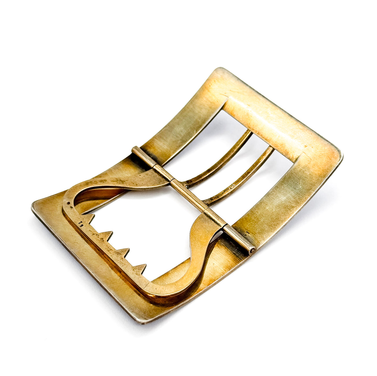 Tilted diagonal view of the gold-washed silver back, the rectangular frame curving away from the corner nearest the viewer while the S-curved tongue and notched bar cross the open centre.