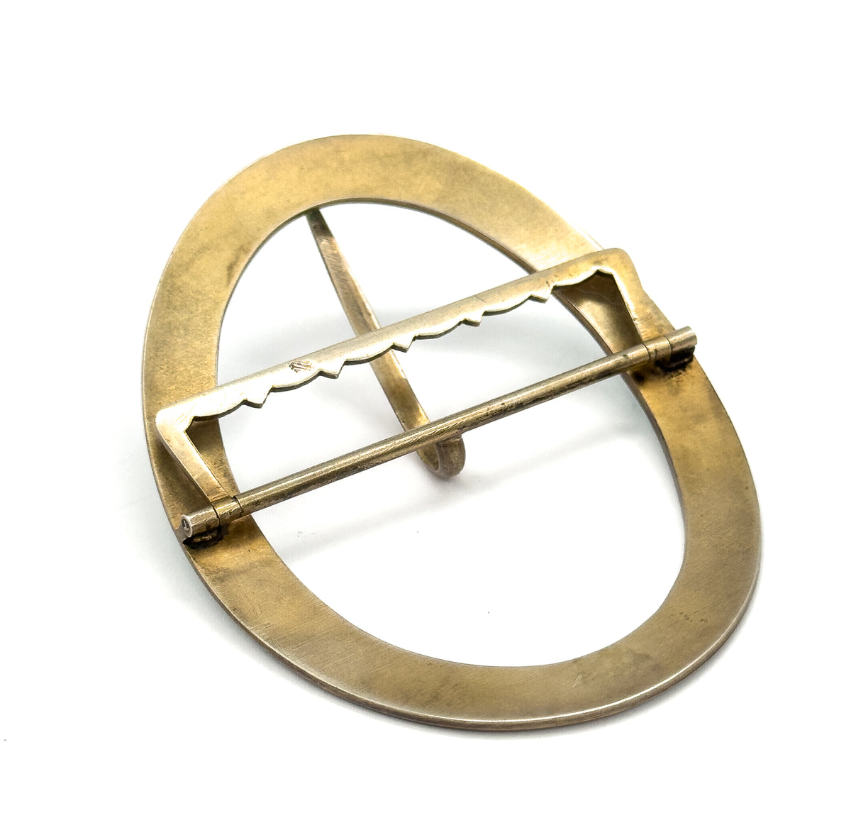 The reverse of the oval buckle, plain gold-wash metal with a scalloped crossbar, hinge pin along one edge and the single prong tucked beneath the centre.