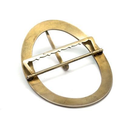 The reverse of the oval buckle, plain gold-wash metal with a scalloped crossbar, hinge pin along one edge and the single prong tucked beneath the centre.