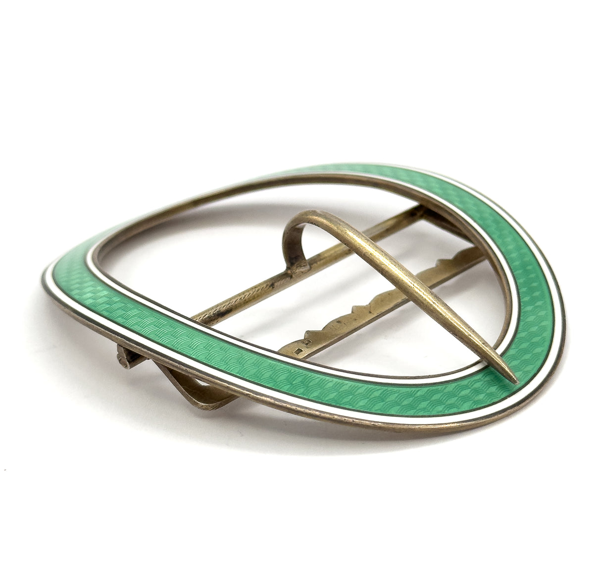Angled three-quarter view from the back, the single prong lying diagonally across the open oval and the scalloped crossbar and hinge visible against the green and white enamel rim.
