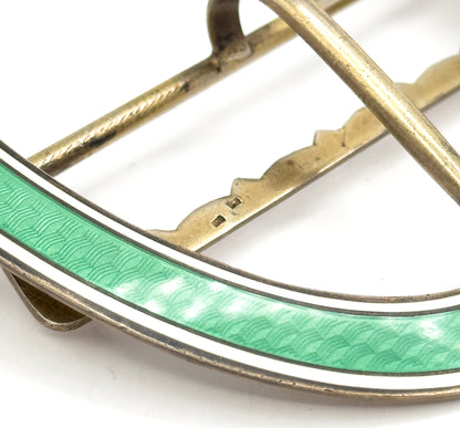 Close macro of the rim where crosshatch engraving glimmers under the transparent green enamel beside its white border, with two tiny hallmarks struck on the scalloped crossbar behind.