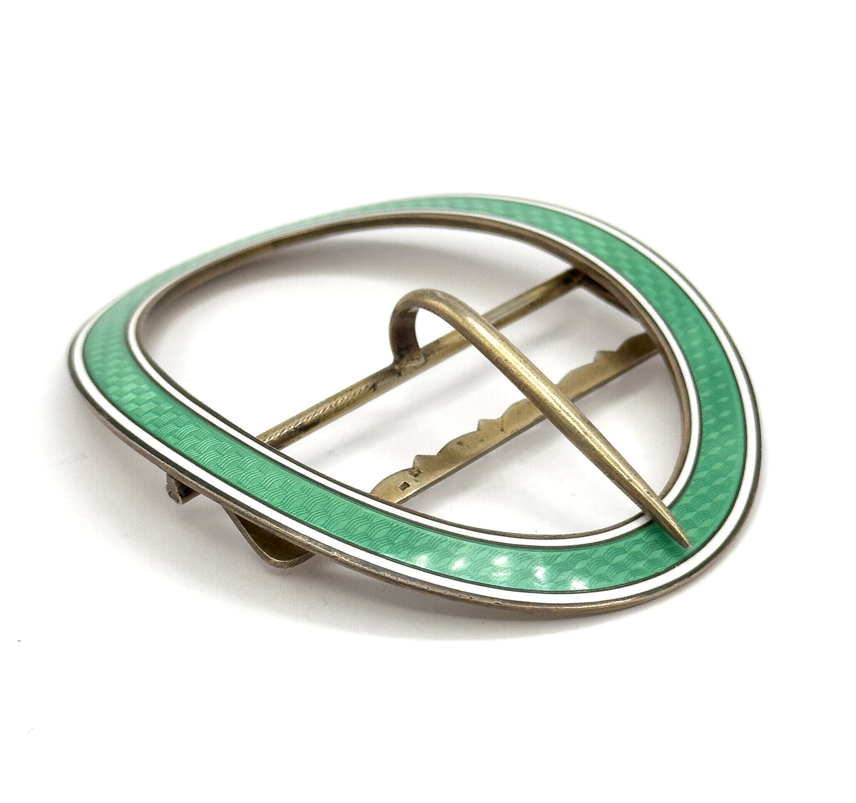 Low tilted view from behind showing the oval frame's slim depth, the prong arching up off the scalloped crossbar, and the green and white enamel rim sweeping around the far edge.