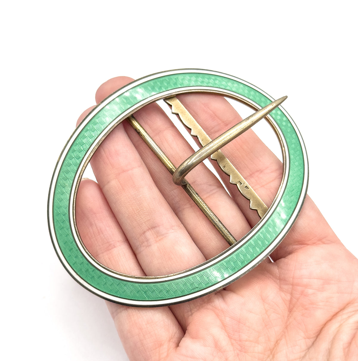 Edwardian sterling silver buckle in mint green guilloche enamel with a white enamel border, shown resting on an open palm that conveys its large oval size, prong crossing the open centre.