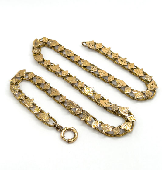 The full chain coiled in a loose S across the surface, the spring-ring clasp swinging free at the bottom and the fan and diamond links repeating along every doubled-back length.