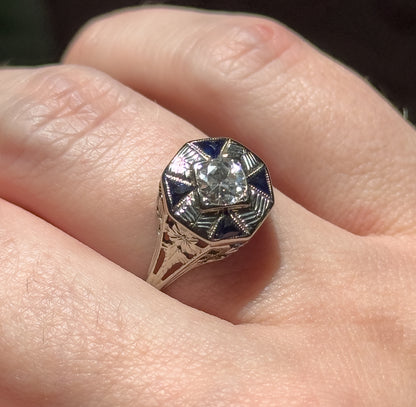 Shown on a finger in daylight, the octagonal face raised above the knuckle so the etched shoulders and pierced filigree gallery along the tapering shank are visible.