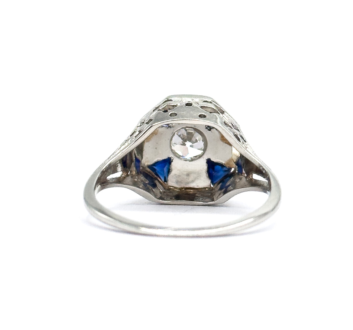 Underside view through the gallery opening, the Old European Cut diamond visible from behind its bezel with two triangular blue stones flanking it and the pierced filigree arching above.