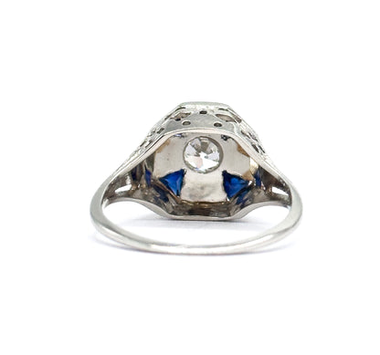 Underside view through the gallery opening, the Old European Cut diamond visible from behind its bezel with two triangular blue stones flanking it and the pierced filigree arching above.