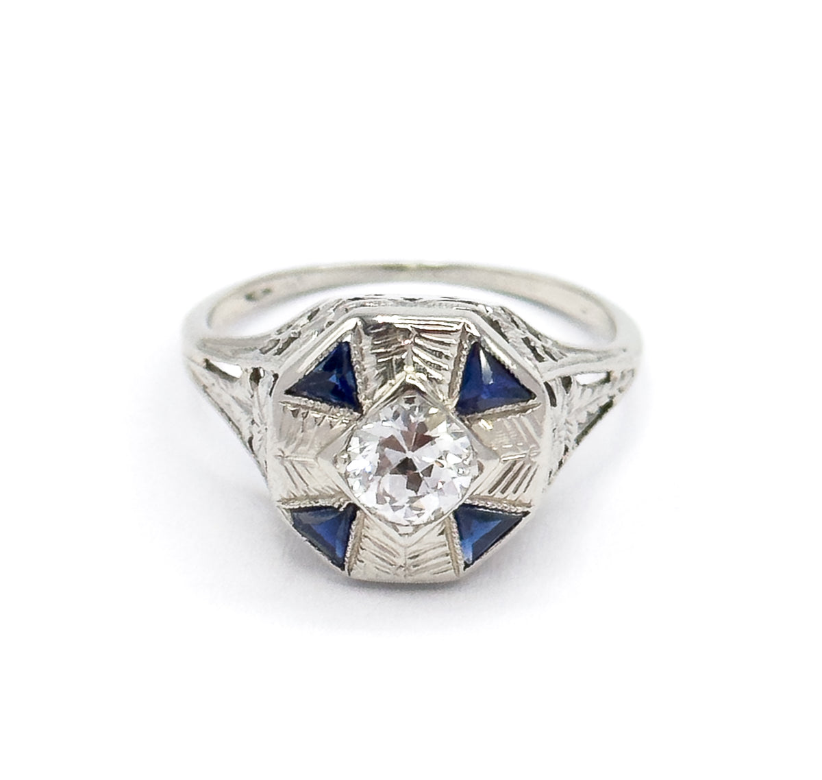 Straight-on overhead view on white, the octagonal face square to the camera so the Old European Cut diamond sits centred within four triangular blue stones and etched rays.