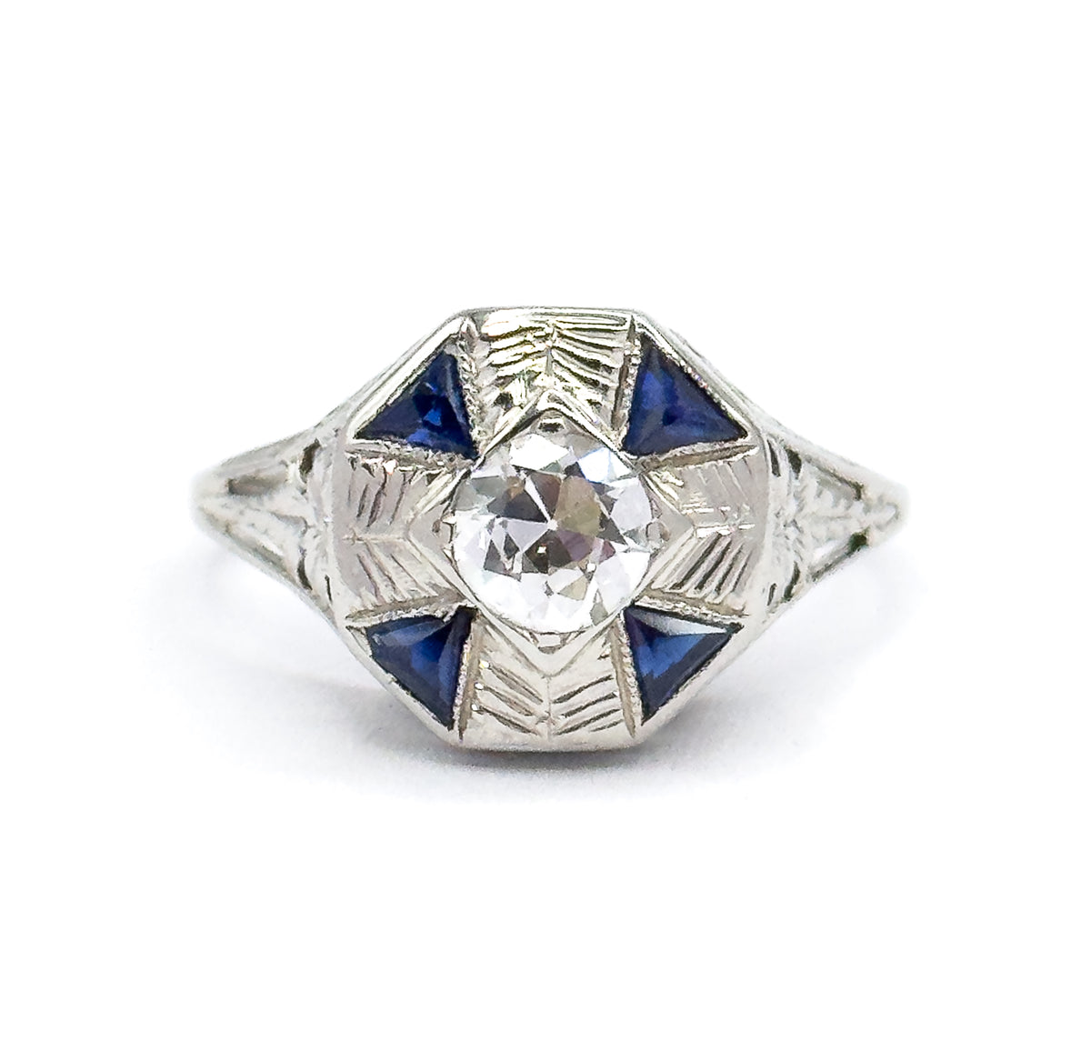 Art Deco diamond and synthetic sapphire ring in 18K white gold, shown face-up against white, the Old European cut diamond centred in an octagonal face with four triangular blue stones.