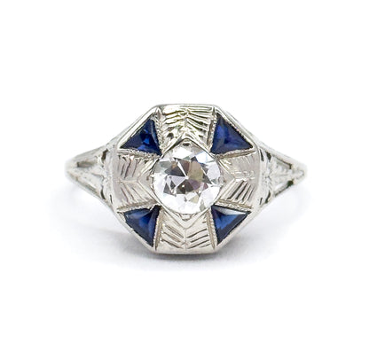 Art Deco diamond and synthetic sapphire ring in 18K white gold, shown face-up against white, the Old European cut diamond centred in an octagonal face with four triangular blue stones.