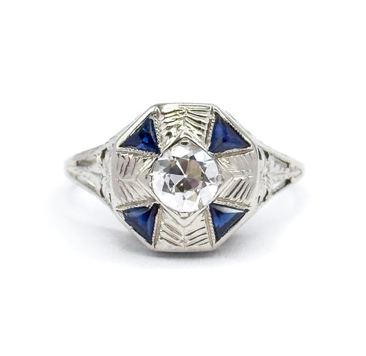 Art Deco diamond and synthetic sapphire ring in 18K white gold, shown face-up against white, the Old European cut diamond centred in an octagonal face with four triangular blue stones.