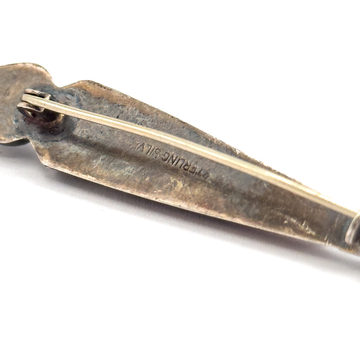 Reverse of the brooch, showing the long pin stem running from its hinge at the left down the back of the body, with a "STERLING SILVER" stamp impressed in the patinated metal.