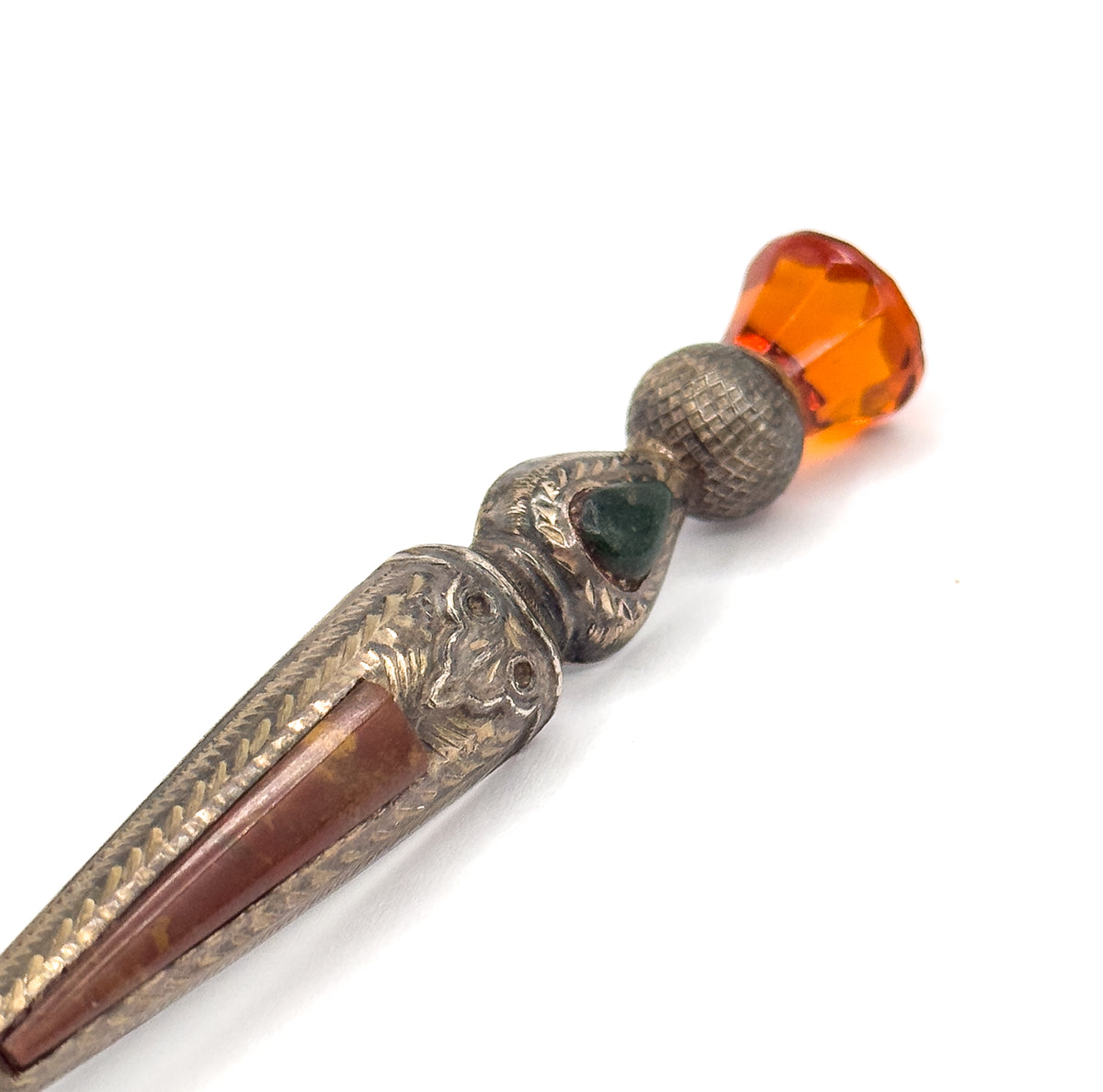 Diagonal view along the front, the reddish-brown agate inlay in the tapering body leading up past a small green agate triangle to the cross-hatched bulb and faceted orange glass at the top.