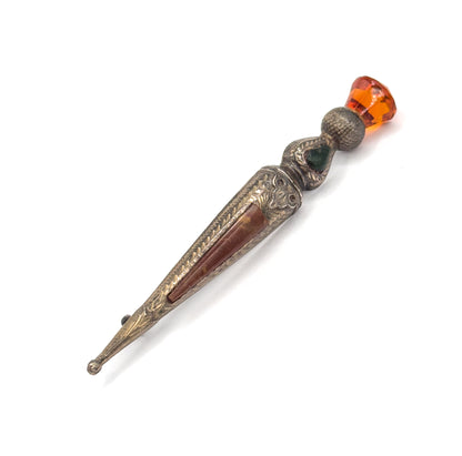Full length of the pin laid diagonally across white, from the small rounded ball at the lower tip up through the agate-inlaid tapering body to the faceted orange glass at the top.