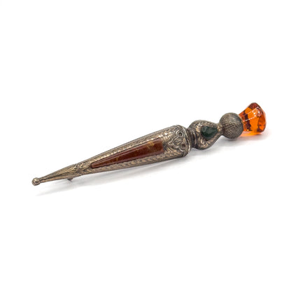 Steeply tilted view from above, catching the engraved leaf detail along the edges of the tapering body and the small ball terminal, with the pin stem peeking out behind the shank.