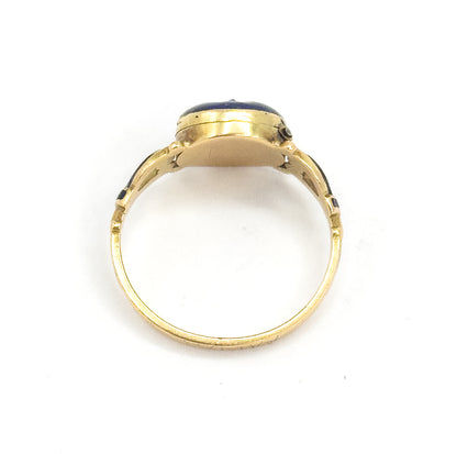 Looking straight through the circle of the shank from behind, the closed locket case sits at the top with just a sliver of its blue enamel face visible above the openwork shoulders.