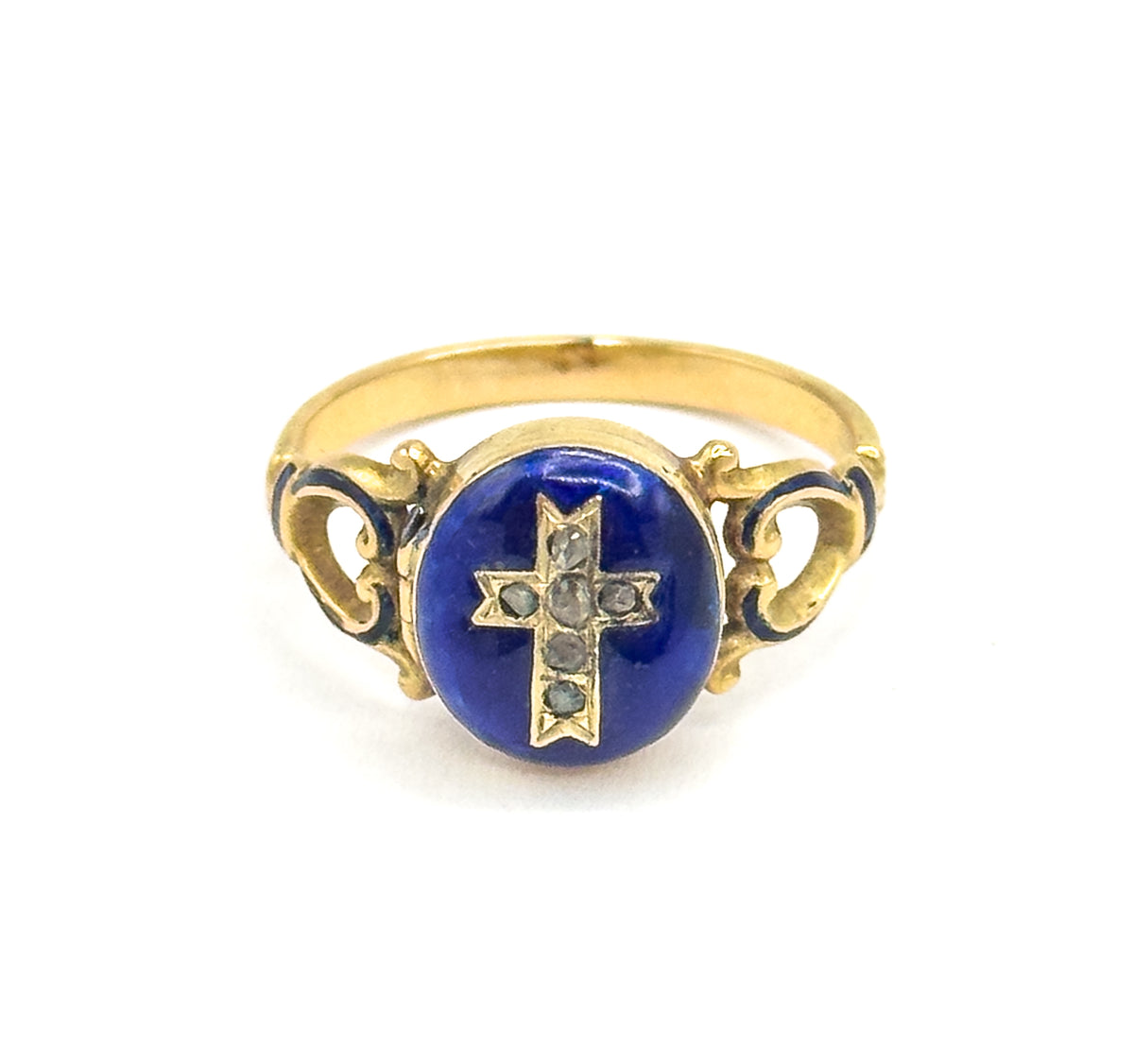 Straight-on front view with the ring upright, the round blue enamel face centred and its cross of six small faceted stones facing the camera, scrolled openwork shoulders flanking it and the shank arching above.