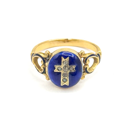 Straight-on front view with the ring upright, the round blue enamel face centred and its cross of six small faceted stones facing the camera, scrolled openwork shoulders flanking it and the shank arching above.