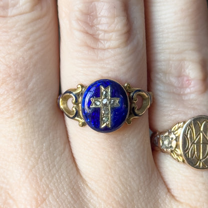 Closer crop of the ring shown on a finger, filling the frame so the scrolled gold shoulders and the six small rose cut diamonds forming the cross on the blue enamel face read clearly.