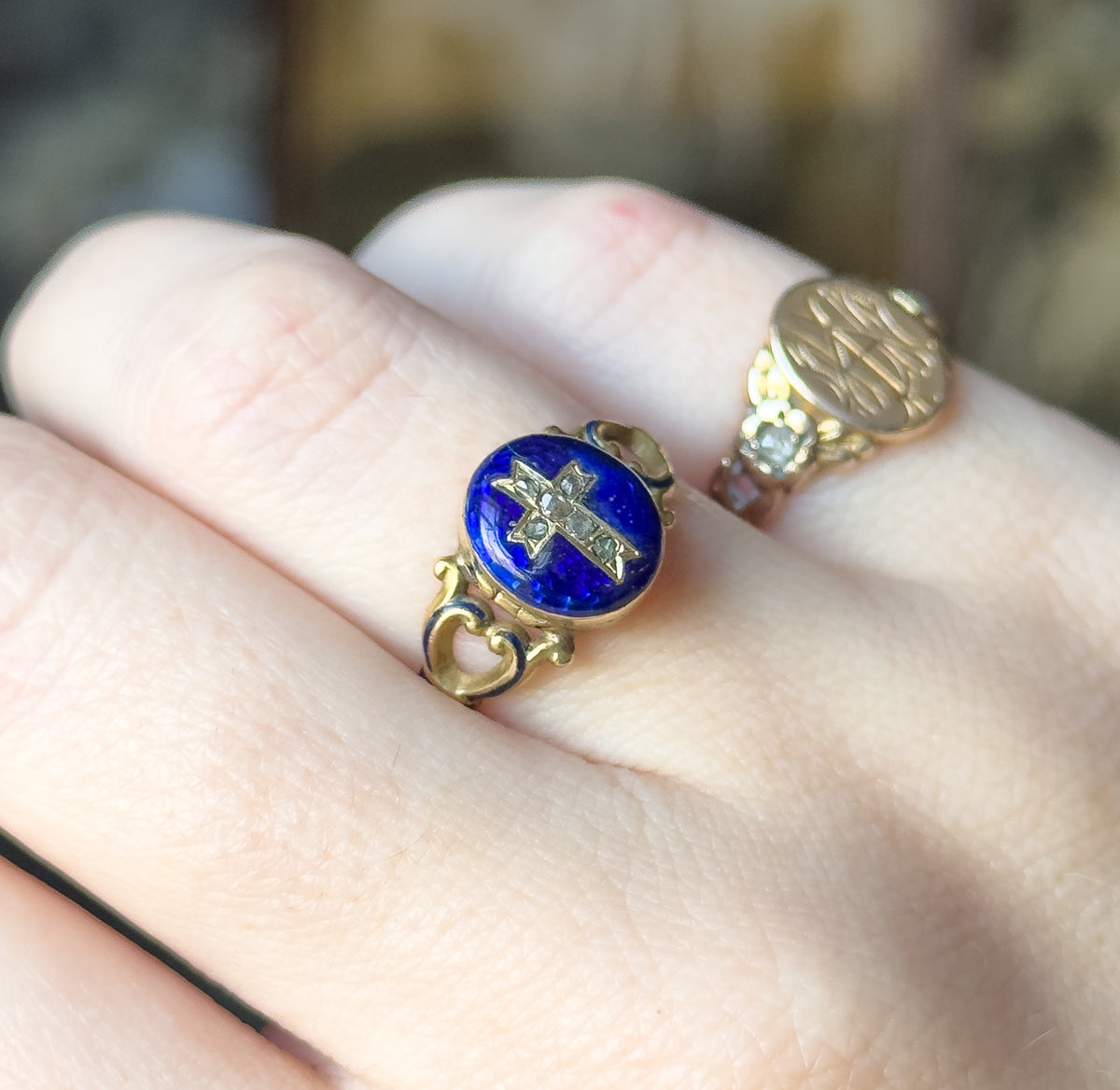 Angled view from above the knuckles, the oval face tilted so its raised bezel and the enamelled scroll shoulders catch the light, with a second gold ring on the next finger.