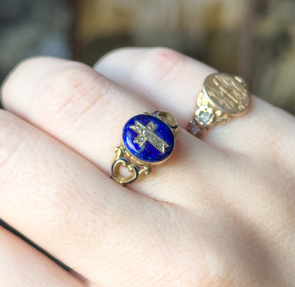 Angled view from above the knuckles, the oval face tilted so its raised bezel and the enamelled scroll shoulders catch the light, with a second gold ring on the next finger.