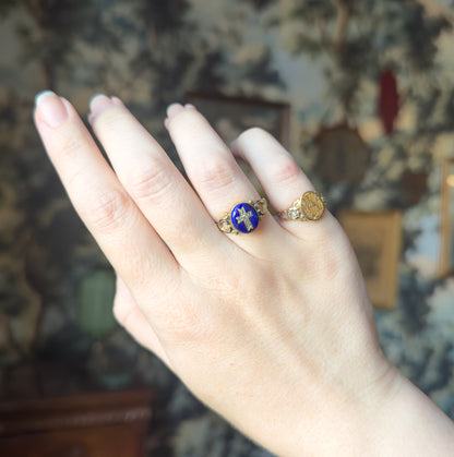 Full view of the raised hand against a patterned backdrop, the whole hand in frame giving a sense of the ring's small scale beside the signet-style gold ring on the next finger.
