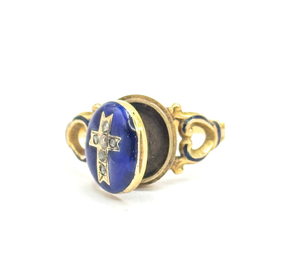 Side view off the hand against white, the hinged enamel face with its diamond cross swung open to show the dark recessed compartment behind, between the scrolled openwork shoulders.