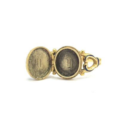 Close view from the side with the locket fully open, both oval interiors facing the camera either side of the small hinge, the scrolled shoulder and blue enamel band trailing off to the right.