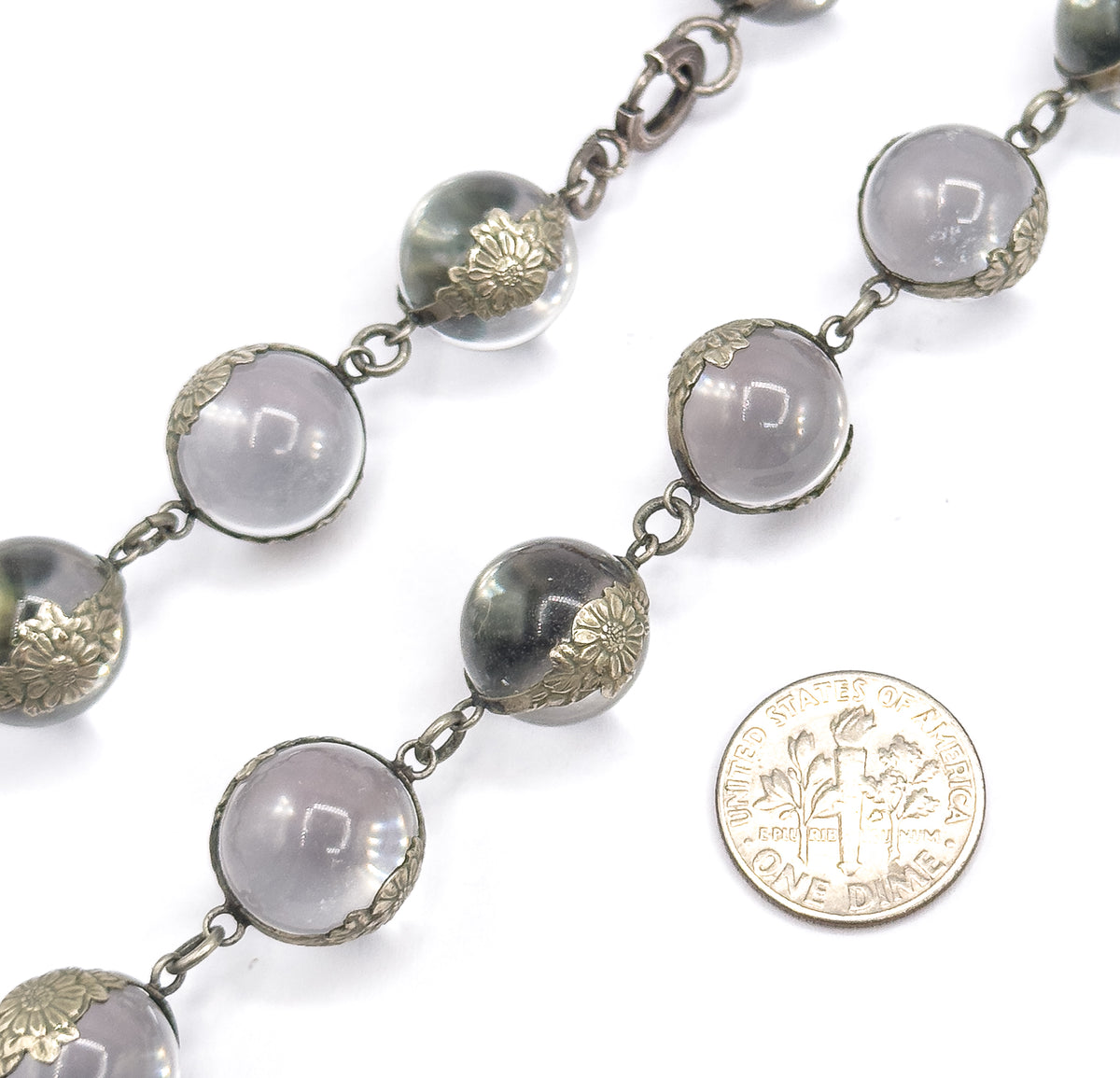 A coin laid beside the strand shows scale — each rock crystal orb in its floral silver mounting is roughly two-thirds the coin's width, with a clasp ring visible at top.