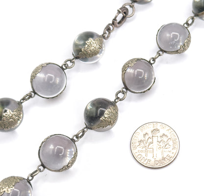 A coin laid beside the strand shows scale — each rock crystal orb in its floral silver mounting is roughly two-thirds the coin's width, with a clasp ring visible at top.