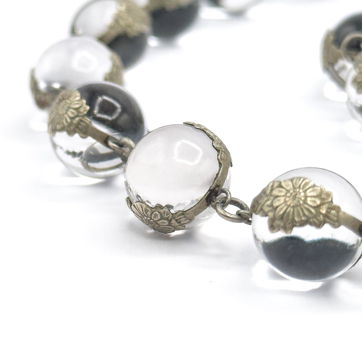Extreme close-up of two adjoining orbs, where the chased floral silver caps can be seen gripping each undrilled rock crystal sphere and a small jump ring joins one mounting to the next.