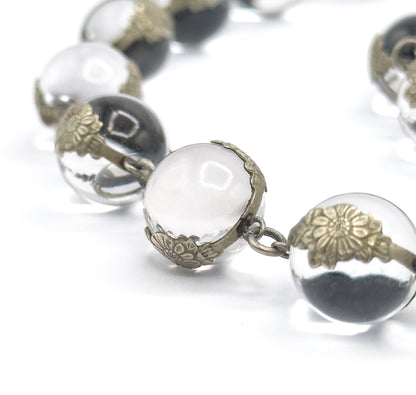 Extreme close-up of two adjoining orbs, where the chased floral silver caps can be seen gripping each undrilled rock crystal sphere and a small jump ring joins one mounting to the next.