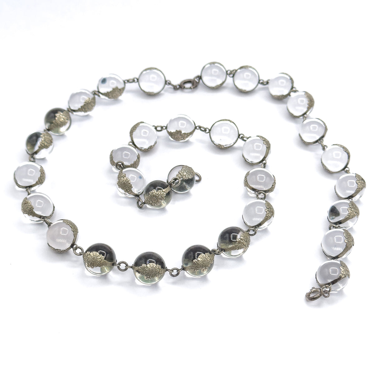The whole strand coiled into a loose spiral on white, both sterling silver clasps visible at opposite ends, letting the full run of 32 orbs in floral mountings be counted in one view.