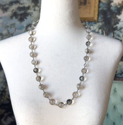 Art Deco pools of light rock crystal necklace in sterling silver, shown at the neck on a cream dress form, its row of round clear orbs held in floral silver mountings with a small clasp at one side.