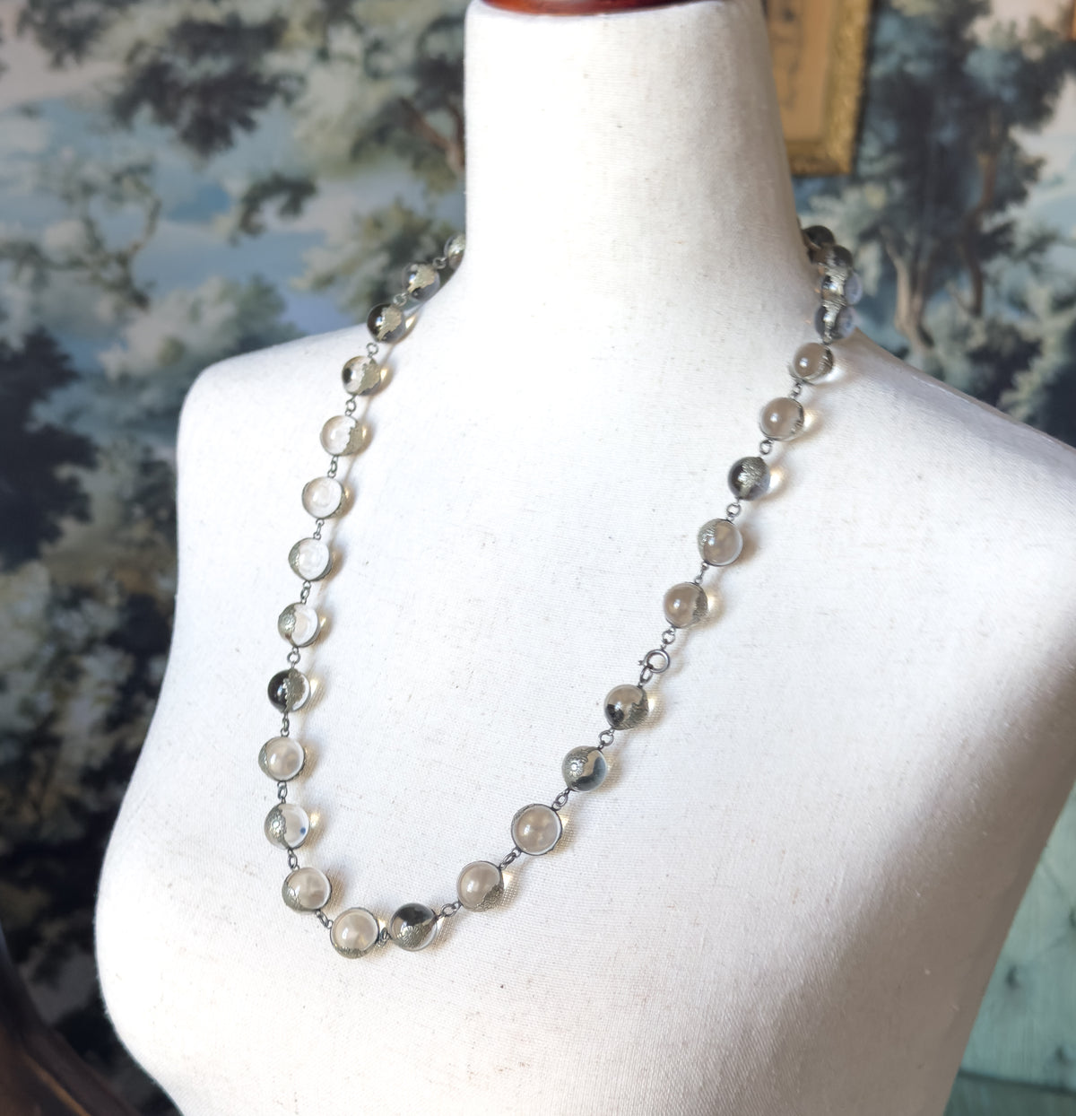 Angled view down onto the dress form, the single long strand curving from the shoulder across the chest with a small ring clasp visible at the right side and each orb in its floral mounting.