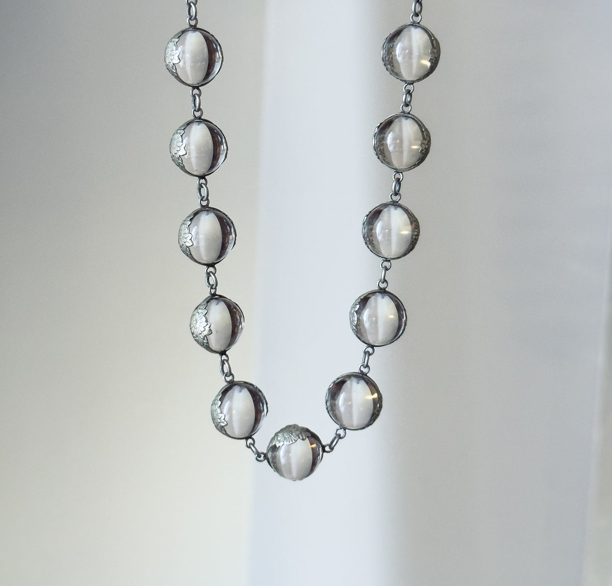 The lower U of the strand hanging free against a pale draped backdrop, each clear orb linked to the next by short silver links and gripped in its floral mounting.