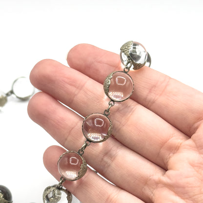 Close macro across the fingers, four orbs filling the frame so each floral silver mounting and the tiny links between them are clear, one orb spanning nearly a finger's width.