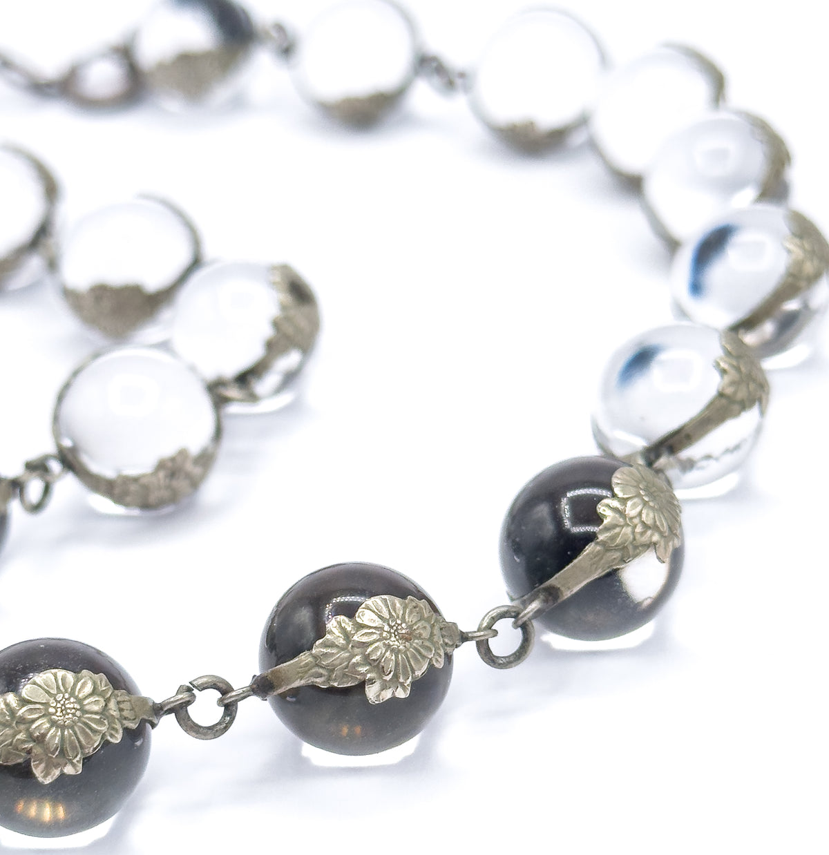 Curving line of orbs on a white background, the nearest spheres reflecting dark in their floral silver mountings while the links and jump rings between them show clearly up close.