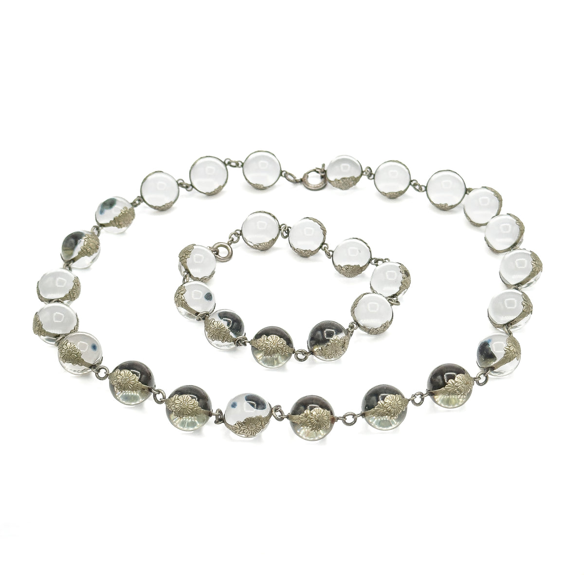 Laid flat on white and separated at its two clasps into a larger oval loop with a smaller bracelet loop nested inside it, every rock crystal orb in its floral silver mounting visible.
