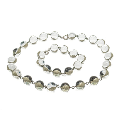 Laid flat on white and separated at its two clasps into a larger oval loop with a smaller bracelet loop nested inside it, every rock crystal orb in its floral silver mounting visible.