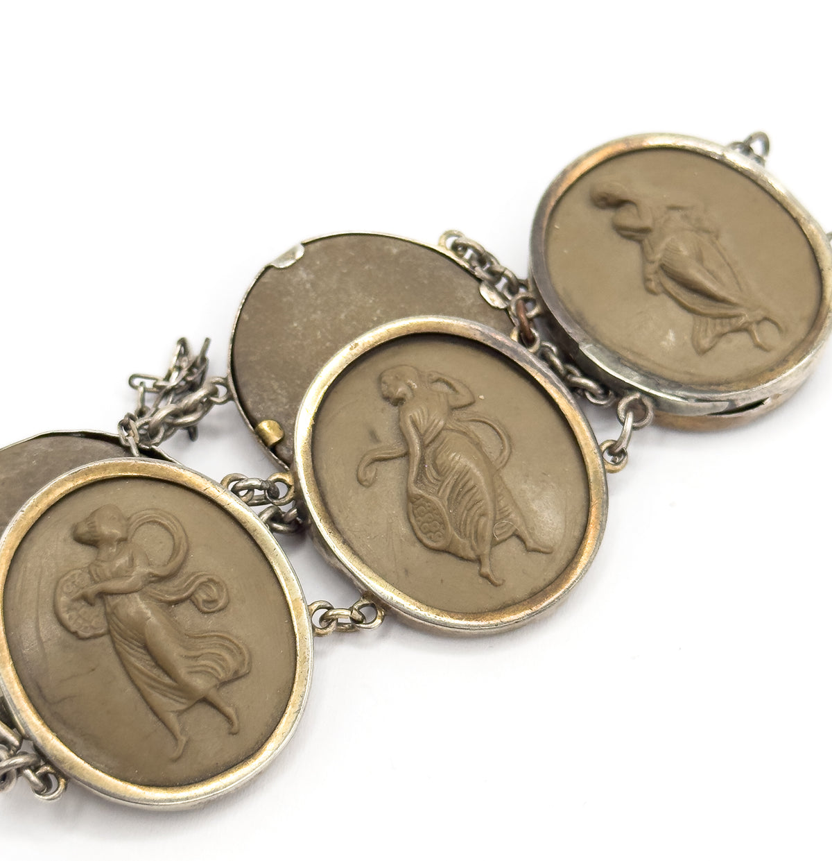 Angled view along four linked bezels in which one cameo is turned away to show its plain blank back, the others carved with draped figures, round links and safety chain running between them.