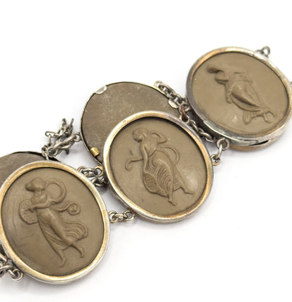 Angled view along four linked bezels in which one cameo is turned away to show its plain blank back, the others carved with draped figures, round links and safety chain running between them.