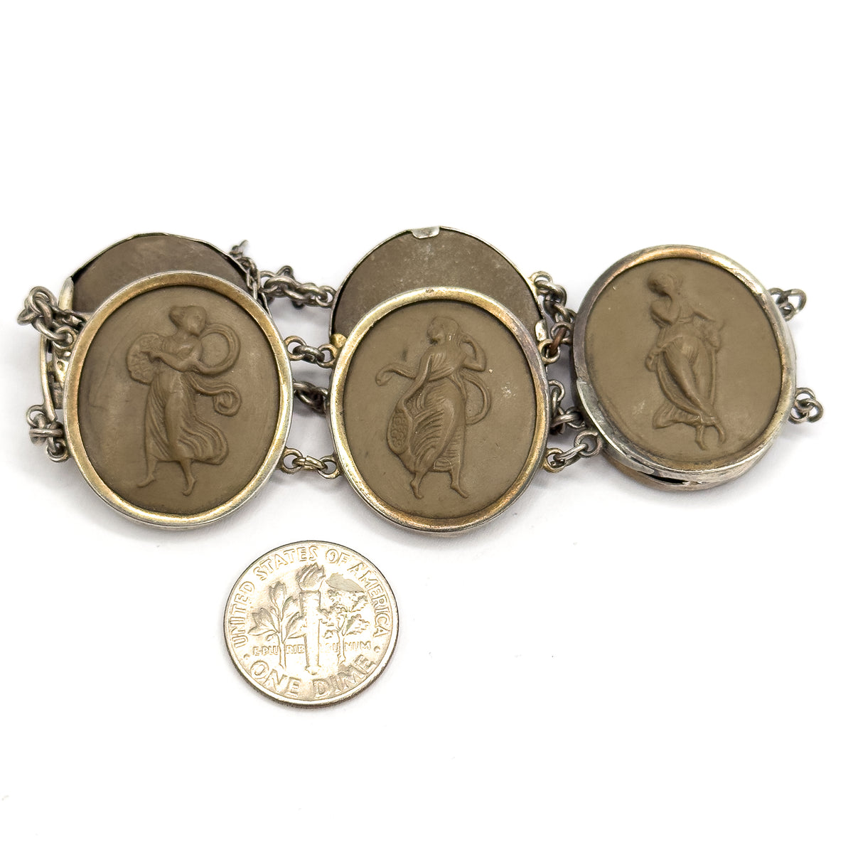 A US dime laid below the row for scale, each carved khaki-brown cameo in its bezel standing roughly twice the coin's width, link chain and safety chain running between them.