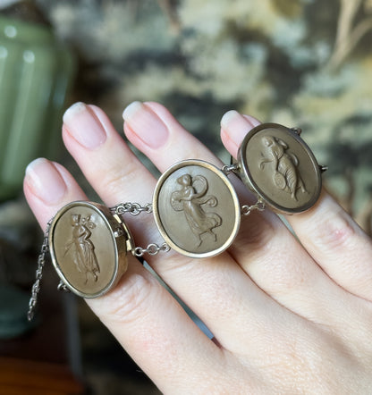 Victorian lava cameo bracelet, its oval khaki-brown carved cameos in bezel frames with prong backs, draped across the fingers of a hand with the safety chain hanging free.
