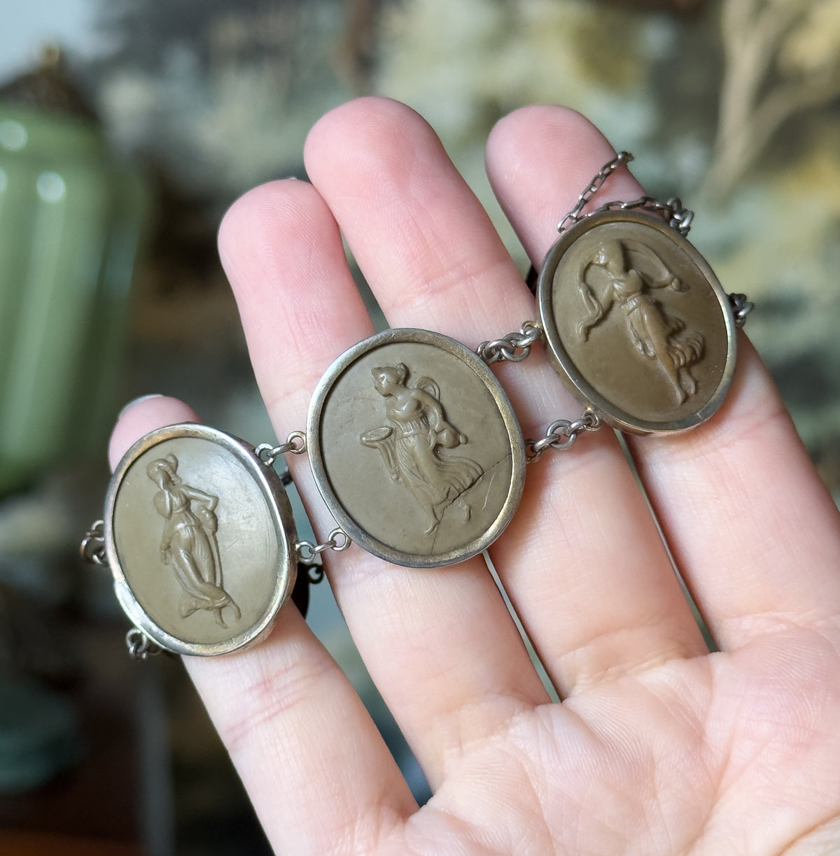 Close view across the palm showing three of the oval cameos, each carved with a standing classical figure, joined by chain links between their bezel frames.